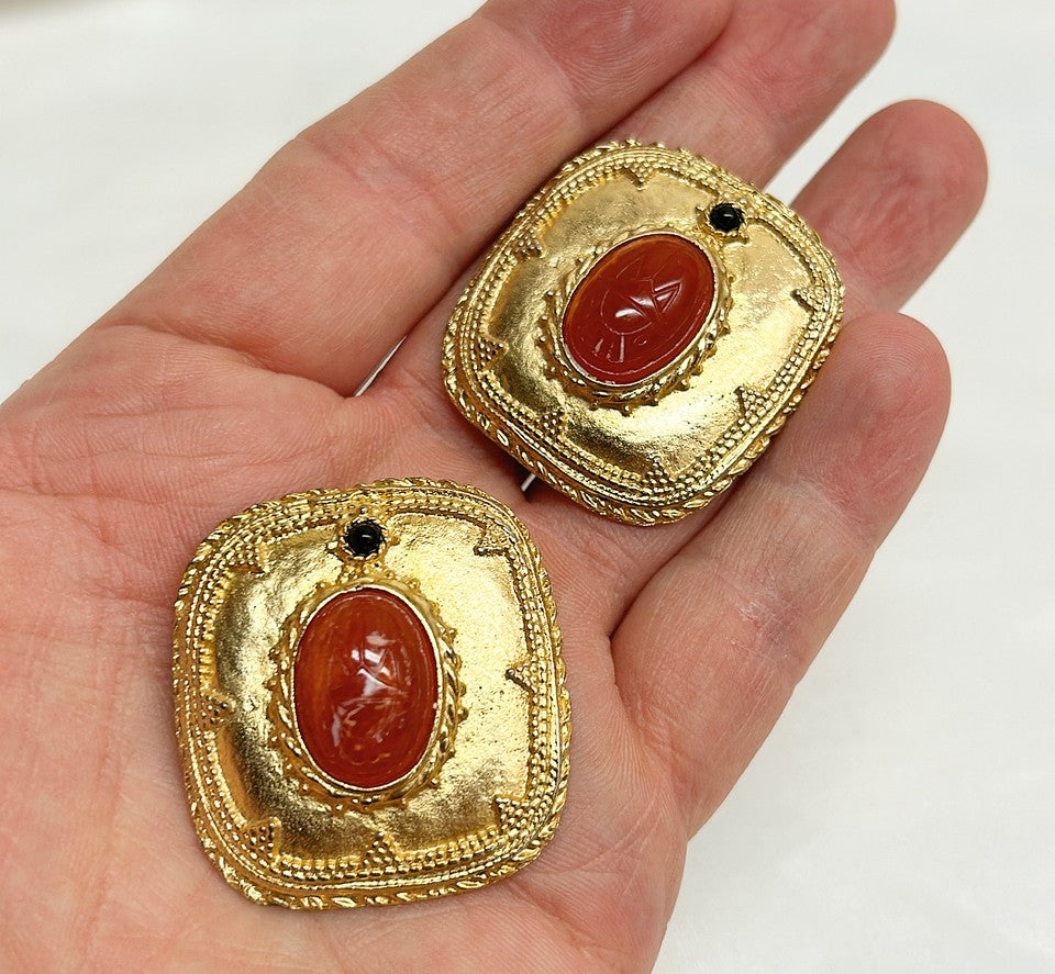 Fabulous statement size 1980s clip on designer style earrings with orange / coral scarab etched center stone.